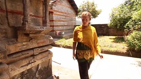 Young woman walks around traditional ancient Krishna Hindu temple in India, slow motion tracking shot, front view