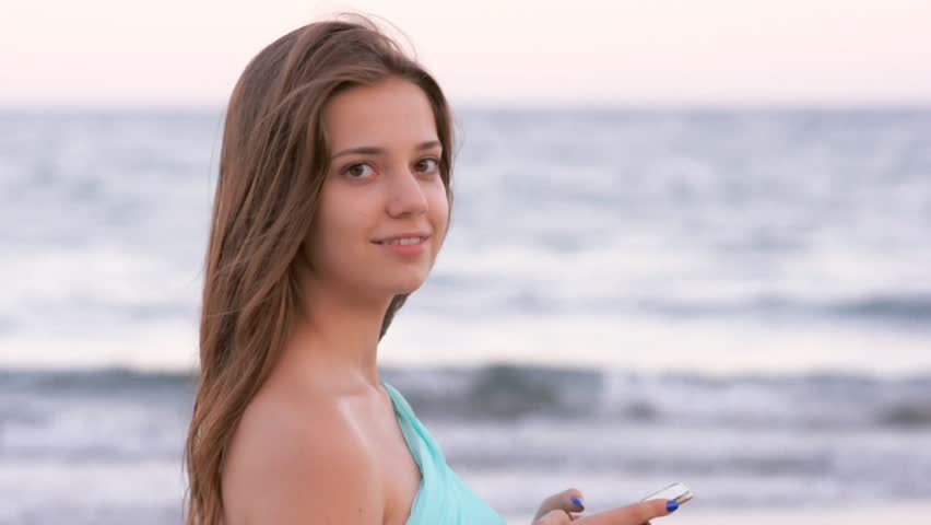 young woman stays at sea beach holding and lookin at smartphone
