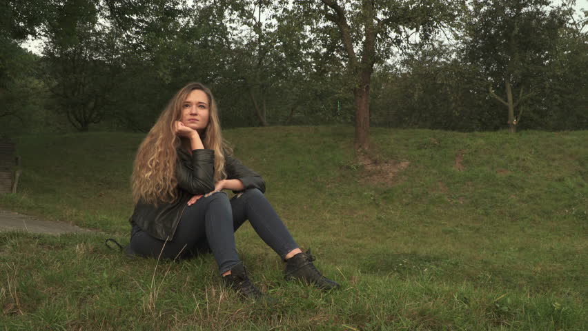 Girl sitting and looking at sunrise then turning toward the camera with a smile, in "Petrin" park in Prague. 
