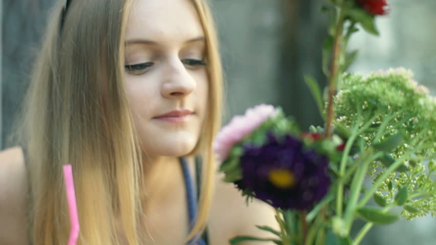 Happy girl smelling flowers in the outdoor cafe and looking thoughtful
