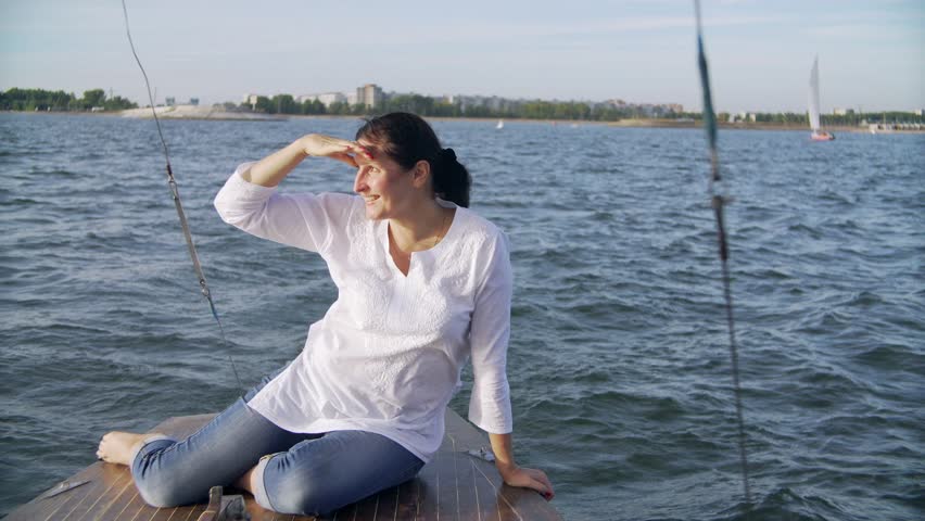 the woman pours from a thermos.  the happy woman sits on the deck of the wooden yacht.