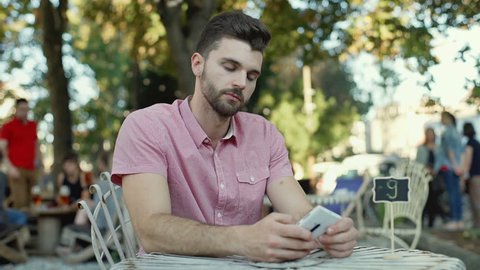 Angry man looking around and checking time on smartphone outdoors

