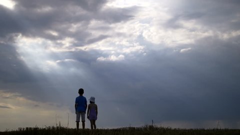 Boy With Girl Walking and Holding Hands on a Background of Clouds at Sunset