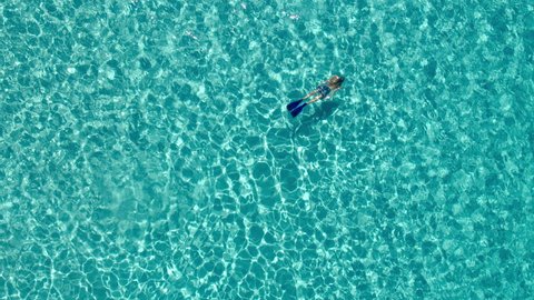 Aerial - High angle view of young woman in board shorts snorkeling underwater in crystal clear waters of luxury travel destination