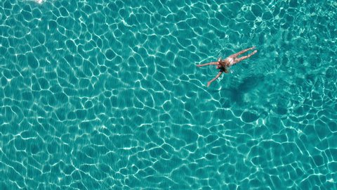Aerial - Beautiful young woman in white bikini enjoys swimming in crystal clear waters