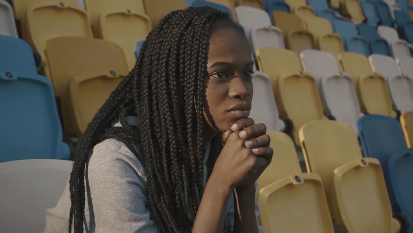 Young african american girl sitting on tribune and looking the match
