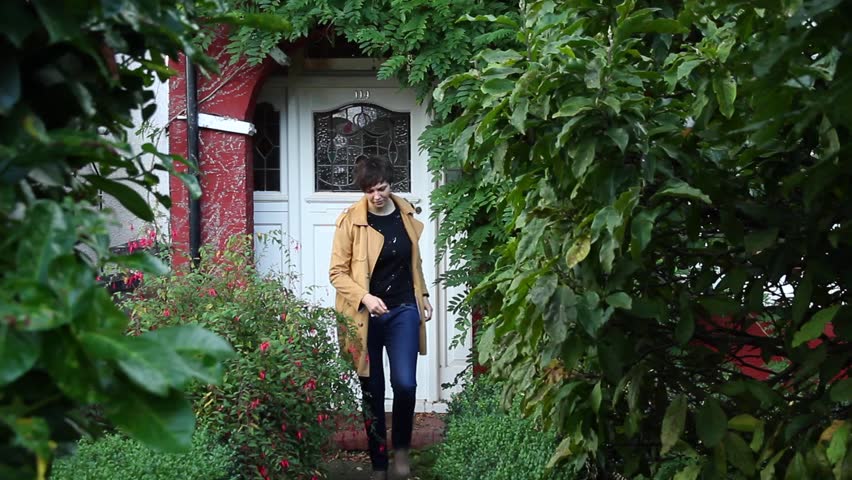 Girl in a yellow coat starts to move away from the door of his house, passing through the garden