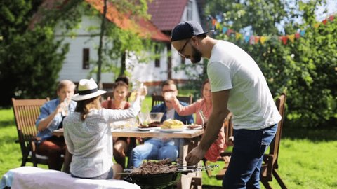 leisure, food and drinks, people and holidays concept - happy man grilling meat on barbecue party for his friends and drinking beer from bottle at summer garden