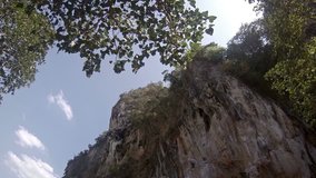 Adventurous tourists take turns climbing the sheer face of a limestone seacliff. towering over a tropical beach paradise in Thailand.