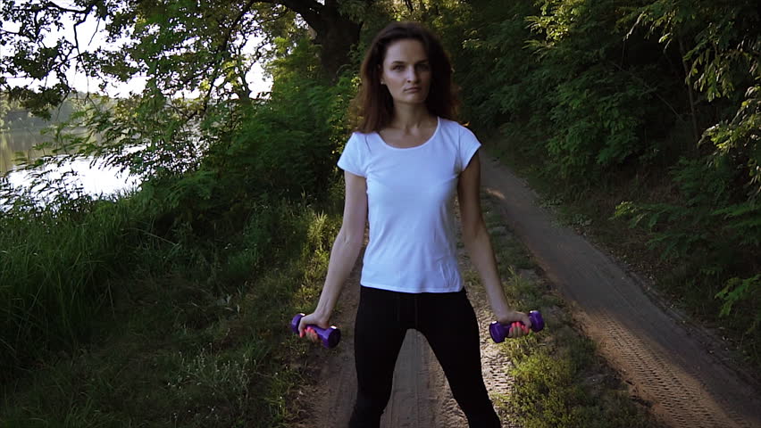 Cheerful girl lifting dumbbells in the park