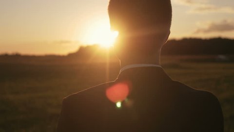 Young man looking forward at the sun during the sunrise. Businessman thinking about business planning.