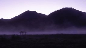 4K zoom out time lapse of misty lake in forest with mountains, hut during sunrise.