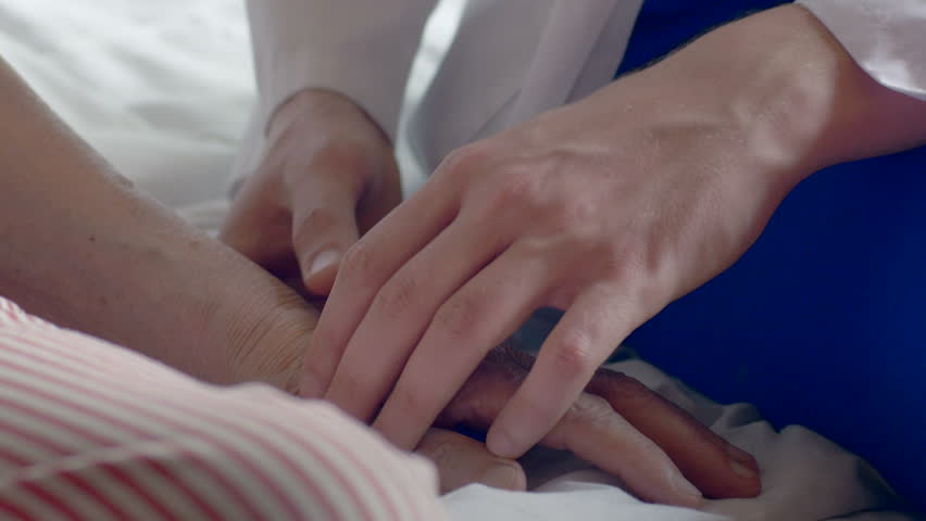 Close-up of a doctor holding a wrinkled hand at the hospital. Man wearing a white coat comforting a weak old patient. Royalty-Free Stock Footage #20129728