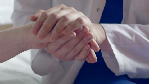 Close-up of a doctor holding a wrinkled hand at the hospital. Man wearing a white coat comforting a weak old patient.