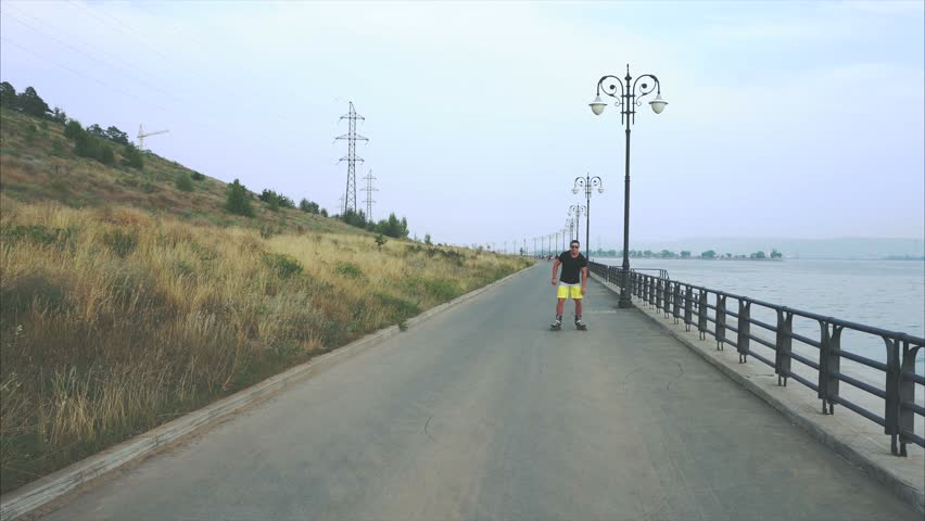 Young sporty man roller skating on summer waterfront 4K