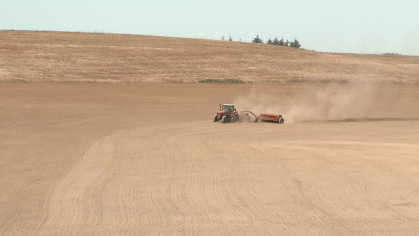 Wide shot of red tractor cultivating soil on farm field in Oregon.