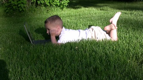 Boy playing on a laptop in the grass and pointing at the screen.  HD 1080i