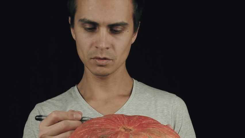 Young men in white t-shirt draws scary face on pumpkin with a marker