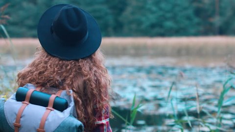 Active healthy Caucasian woman with a backpack taking pictures with an vintage film camera on a forest lake. 4K UHD RAW edited footage