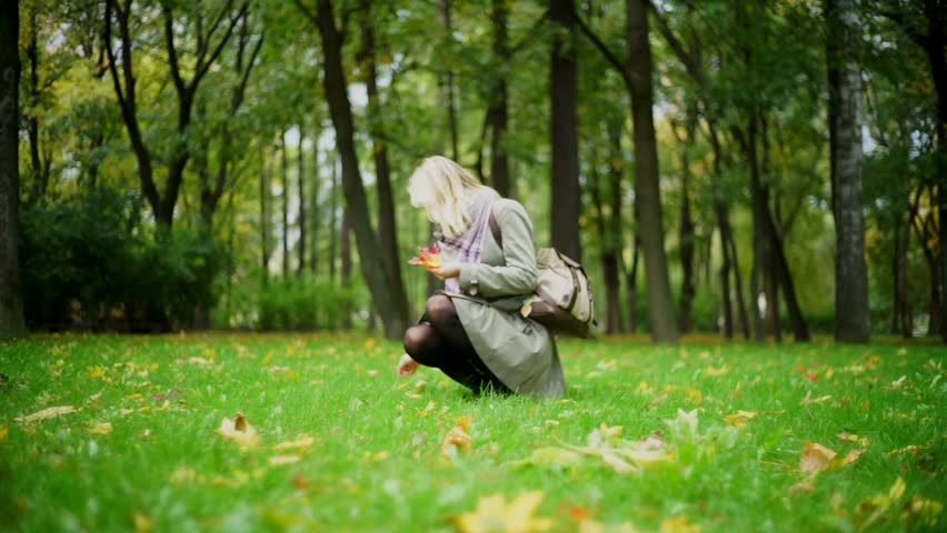 The girl collects fallen leaves in autumn park