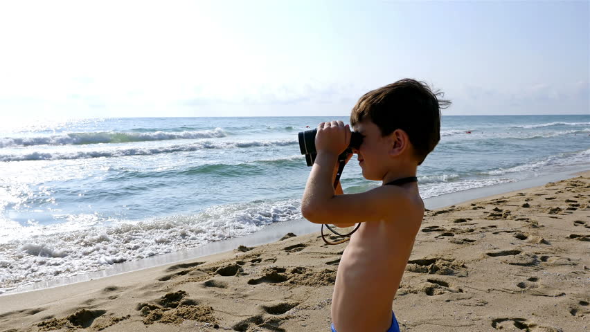 Little boy in swimsuit uses binoculars to explore the sea