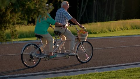 Senior couple riding tandem bicycle. Two people on a bike. Follow the sun. Picking up speed.