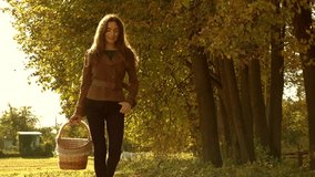 Slow motion steadicam video of a beautiful girl in brown jacket walking through autumn forest carrying a basket