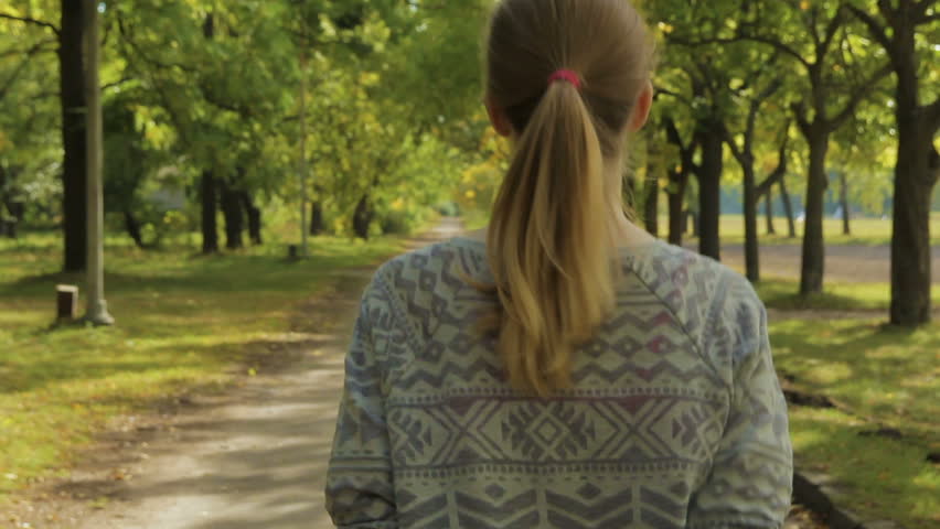 Woman in sun jogging in the park among the trees. Shooting from behind.