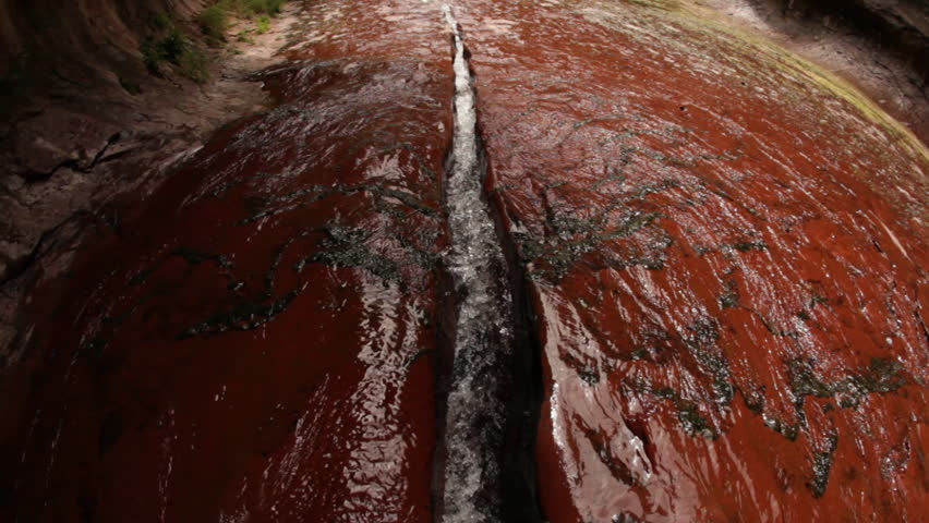 Water stream flows down a red rocky surface