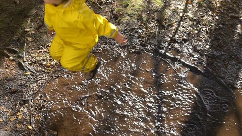 Little girl in a yellow rubber suit is jumping in a puddle. Slow motion.