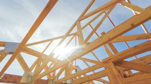 Roof beams of a modern American home in mid construction phase, looking up toward blue sky with sunlight