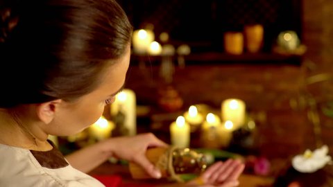Young woman lying on wooden spa bed. Massage in spa salon with masseuse. Masseuse pouring oil in his hand and begins to massage. Girl on candles background in massage spa salon. 4k.
