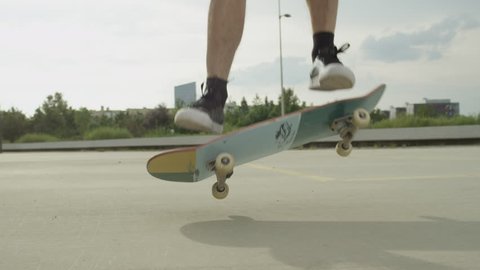 SLOW MOTION CLOSE UP: Unrecognizable skateboarder skateboarding and jumping ollie tricks on street. Extreme closeup of skateboarder's legs and sneakers jumping flip trick with skateboard outdoors.