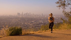 Fit woman Jogging through a park in the Hollywood Hills at sunrise. Hollywood hills and the rising sun can be seen in the background. Slow Motion.