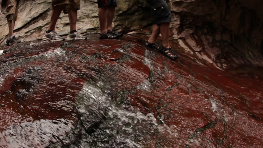 Adventurers walk over a rock with water flowing over its surface.