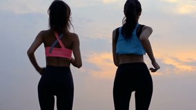 Back view of two beautiful young sports women jogging on beach
