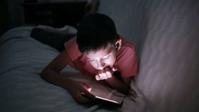 Young boy playing with a cellphone or smartphone on a bed. night