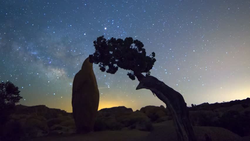 Motion controlled astrophotography time lapse with dolly in, tilt up & zoom out motion of Milky Way galaxy through boulder & cypress tree in Joshua Tree National Park, California