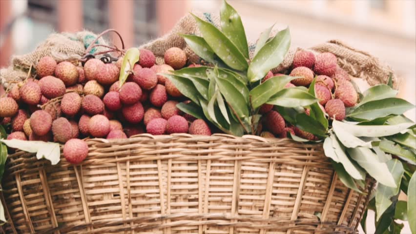 Green grocer carrying a basket of fruits lychee on his head. Closeup.