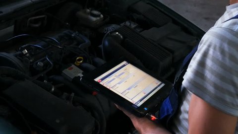 Mechanic in a auto repair shop checking engine using a digital tablet 