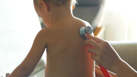 Kid doctor examing little baby boy with stethoscope in a sunny room