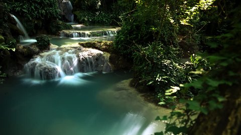 4K Tracking and tilting timelapse of waterfalls with blue and green water with moving shadows and light rays during daytime.