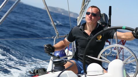 Russian skipper at the helm controls of a sailing yacht during race.