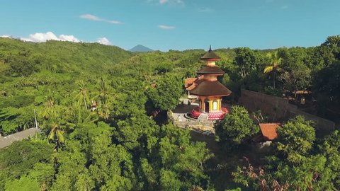 Aerial view of orange temple tower on a green hill, Brahma Vihara Arama Buddhist Monastery, moving forward,