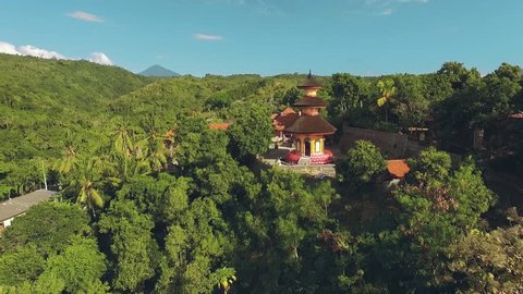 Aerial view of orange temple tower on a green hill, Brahma Vihara Arama Buddhist Monastery, moving forward,