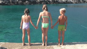 3 children jumping into the sea holding hands. Long Shot, Handheld Shot, slow motion, contains children 8-9 and 10-12 years. Montenegro, Adreatic sea.