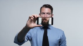Young attractive male having fun with cell phone camera on plain background