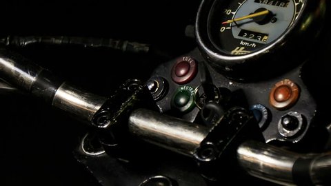 closeup guy hand switches on engine throttle of motorcycle on control board by speedometer against darkness