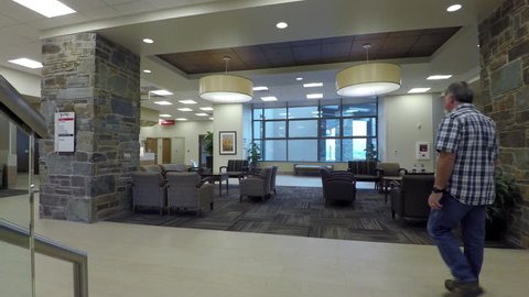 LEHI, UTAH - OCT 2016: Hospital waiting room man walks to laptop computer. Modern new state of the art hospital and medical clinic. Patients and family improve health well being. Healthcare medicine.