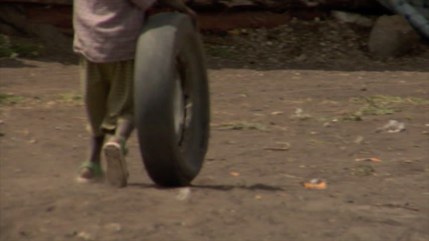 KENYA - CIRCA 2006: Unidentified African boy rolls a tire down a dirt road circa